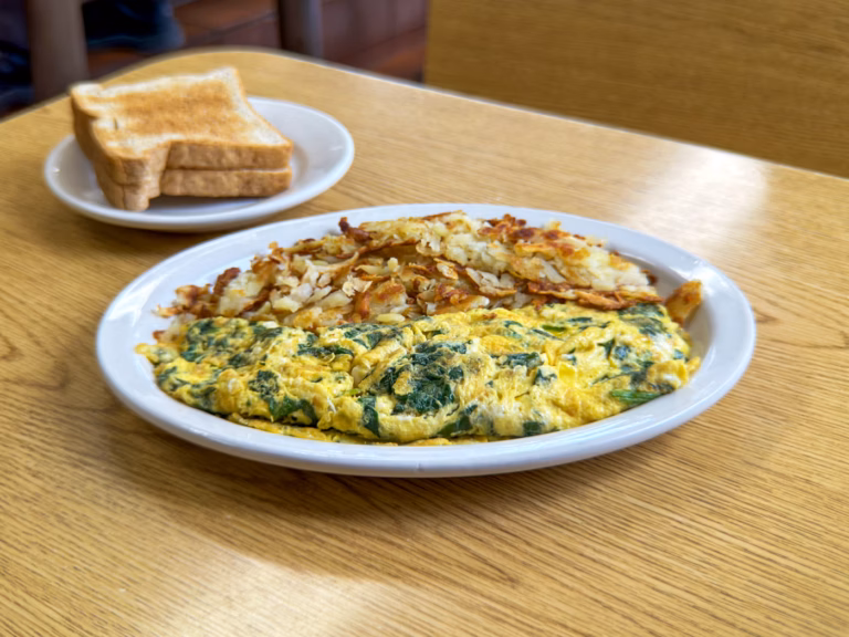A fluffy Northside Grill spinach and feta omelette served with a side of crispy, golden-brown hash browns and two slices of buttered white toast.