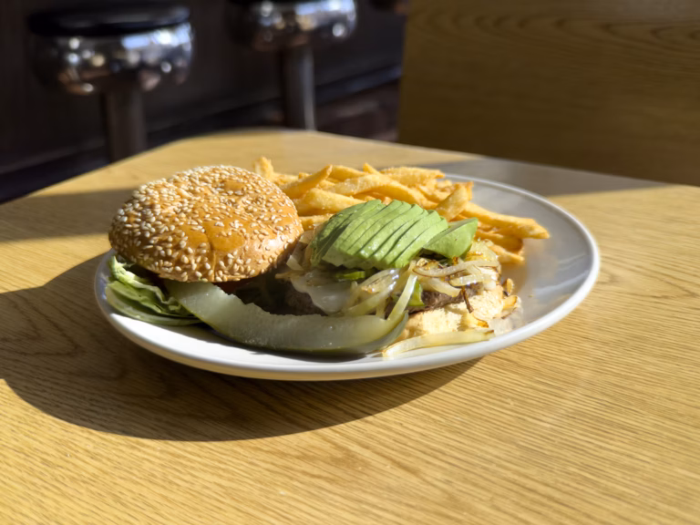 A gourmet Northside Grill avocado burger featuring a juicy beef patty topped with fresh, sliced avocado, melted cheese, lettuce, and onion on a brioche bun.