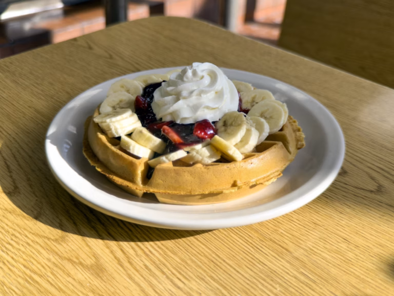 A golden-brown Northside Grill Belgian waffle topped with fresh sliced bananas, a vibrant mixed fruit compote, and a dollop of whipped cream, served fresh in our Irving Park dining room.